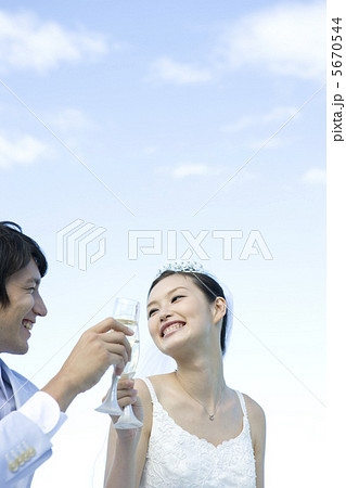 青空の下でグラスを手に乾杯する新郎新婦 5670544
