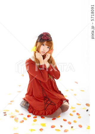 落ち葉の中で座り込む可愛い童顔の女の子の写真素材