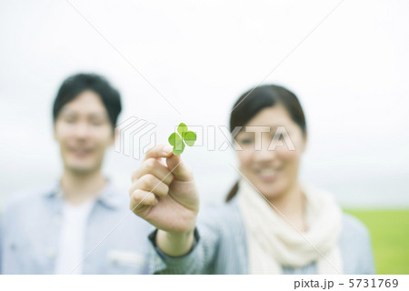 草原で四葉のクローバーを持ち微笑むカップルの手元 5731769