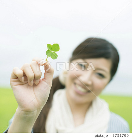 草原で四葉のクローバーを持ち微笑む女性 5731799
