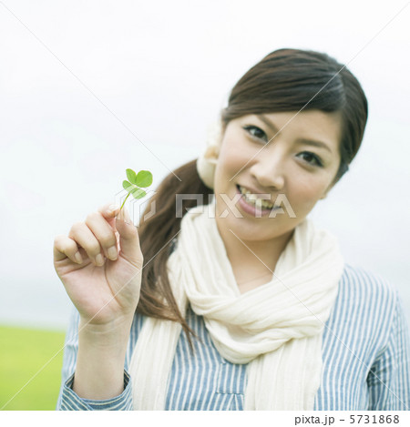 草原で四葉のクローバーを持ち微笑む女性 5731868
