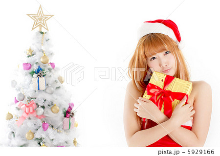 クリスマスツリーと大切そうにクリスマスプレゼントを抱えた可愛いサンタガールの写真素材
