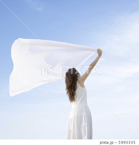 青空の下で布を持って広げる女性の写真素材