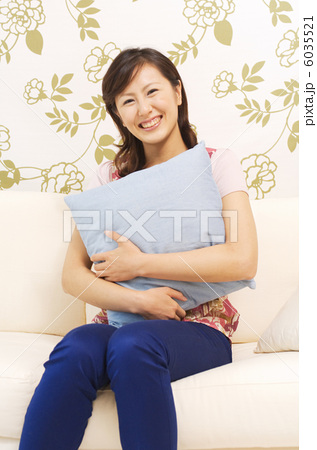 クッションを抱きしめてソファに座る女性の写真素材