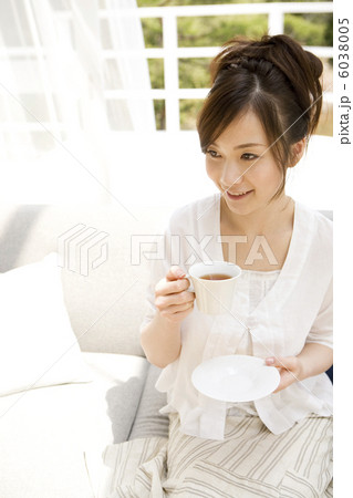 ソファに座ってティーを飲もうとする女性 6038005