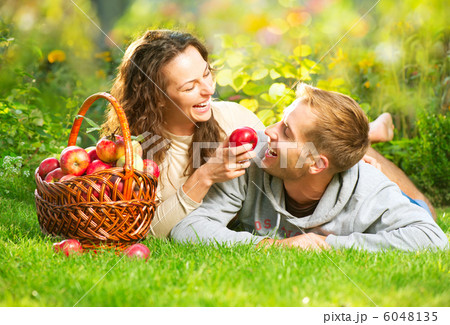 Couple Relaxing on the Grass and Eating Apples in Autumn Garden 6048135