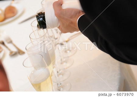 結婚式会場に来てくれたゲストのシャンパングラスにシャンパンを注ぎ、もてなす新郎の手元の写真 6073970