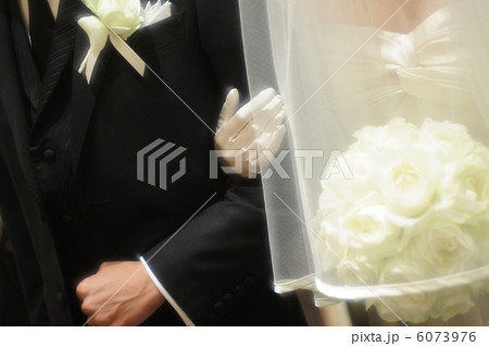 結婚式に腕を組んで登場する、タキシード姿の新郎と純白のウエディングドレス姿の新婦の写真 6073976