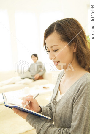 手帳にメモする女性とソファに座る男性 6115644