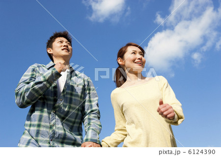 青空と手をつないで走るカップル 6124390