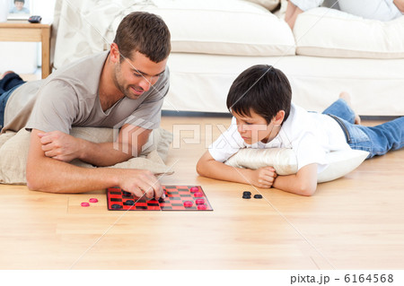 Handsome man playing checkers with his son lying on the floor 6164568