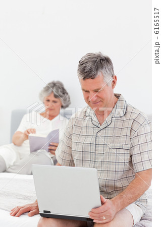 Man working on his laptop while his wife is reading 6165517