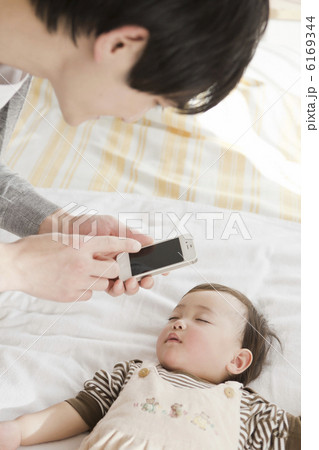 赤ちゃんの寝顔をスマートフォンで撮影する父親 6169344
