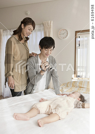 赤ちゃんの寝顔をビデオカメラで撮影している両親の写真素材