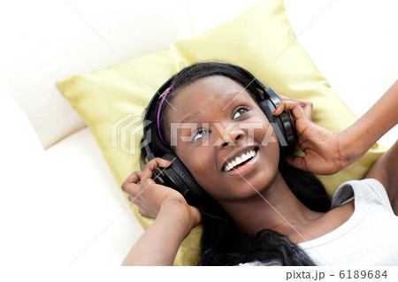 Smiling woman listening music with headphones lying on a sofa Smiling woman listening music with headphones lying on a sofa 6189684