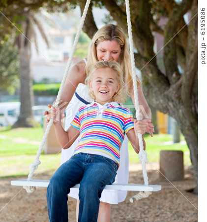 Jolly mother pushing her daughter on a swing Jolly mother pushing her daughter on a swing 6195086
