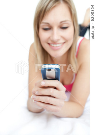 Young woman sending a text lying on a bed Young woman sending a text lying on a bed 6200354