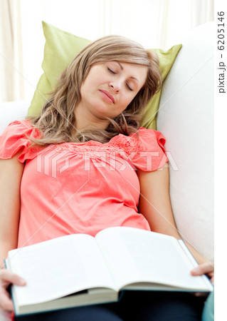 Tired woman reading a book lying on a sofa in the living-room 6205146