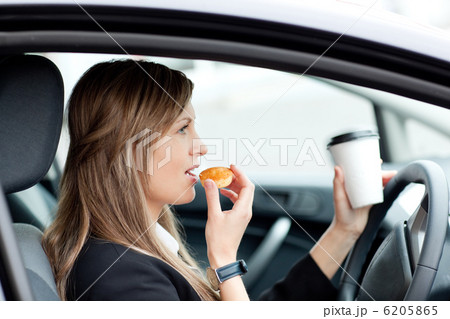 Charming businesswoman eating and holding a drinking cup while d 6205865