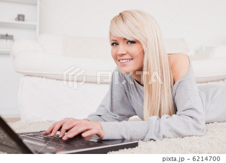 Pretty blond woman relaxing on laptop lying on a carpet 6214700