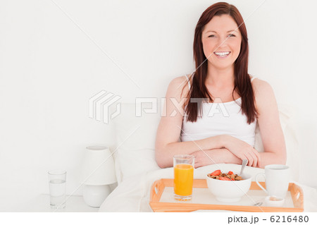 Beautiful red-haired woman having her breakfast while sitting on 6216480