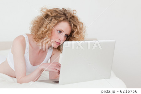 Beautiful blonde woman relaxing with her laptop while lying on h 6216756