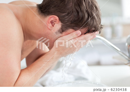 Cute caucasian man spraying water on his face after shaving in t Cute caucasian man spraying water on his face after shaving in t 6230438