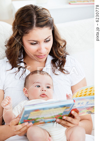 Attentive mother reading a book to her adorable baby sitting in Attentive mother reading a book to her adorable baby sitting in 6230778