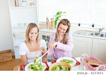 Adorable woman serving salad to her friend sitting at a table du 6231651