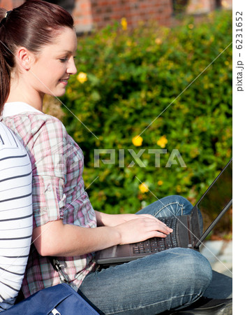 Charming female student using a laptop and sitting behind her bo Charming female student using a laptop and sitting behind her bo 6231652