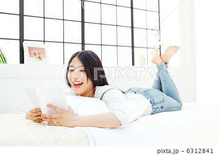 ベッドで寝ながら本を読む女性の写真素材