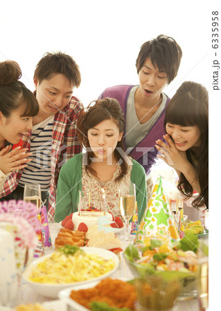 誕生日を祝う男女とろうそくを吹き消す女性 6335958
