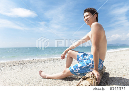 流木に座っている水着姿の男性の写真素材