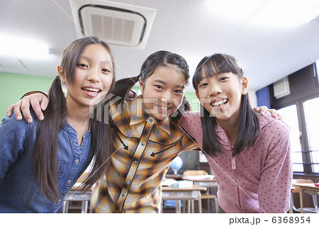 教室で肩を組んでいる小学生の女の子3人の写真素材