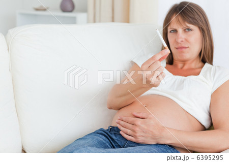 Charming pregnant woman holding a cigarette while lying on a sof 6395295