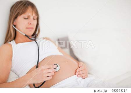 Beautiful pregnant woman using a stethoscope while lying on a be Beautiful pregnant woman using a stethoscope while lying on a be 6395314