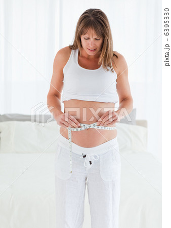 Good looking pregnant female using a tape measure while standing Good looking pregnant female using a tape measure while standing 6395330
