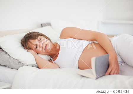 Beautiful pregnant woman reading a book while lying on her bed Beautiful pregnant woman reading a book while lying on her bed 6395432