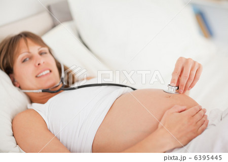 Pretty pregnant woman using a stethoscope while lying on a bed Pretty pregnant woman using a stethoscope while lying on a bed 6395445
