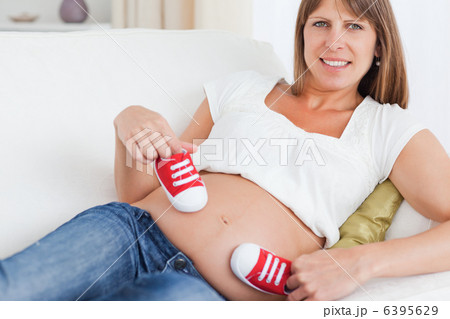 Good looking pregnant female playing with red baby shoes while l Good looking pregnant female playing with red baby shoes while l 6395629