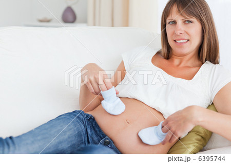 Young pregnant woman playing with baby shoes while lying 6395744