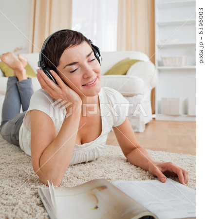 Portrait of a delighted woman with a magazine enjoying some musi 6396003
