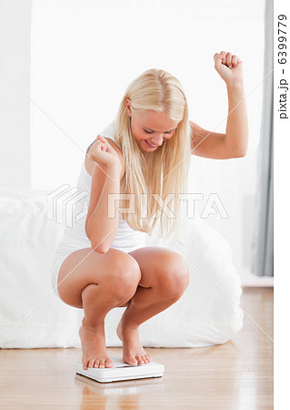 Portrait of a sportive woman squatting on a weighing machine 6399779