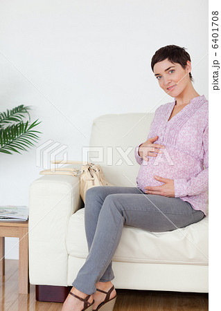 Pretty pregnant woman sitting on a sofa touching her belly 6401708