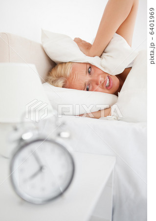 Portrait of a tired woman hidding her head in a pillow while the Portrait of a tired woman hidding her head in a pillow while the 6401969