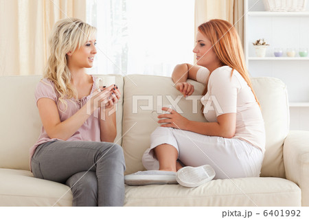 Charming young Women sitting on a sofa with cups 6401992