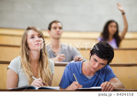 Students taking notes while their classmate is raising her hand 6404358