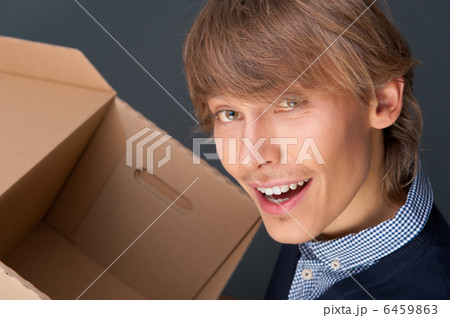 Portrait of young man holding on box against grey wall. He is st Portrait of young man holding on box against grey wall. He is st 6459863