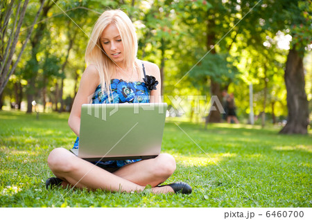 Beautiful student woman with a laptop sitting on green grass at 6460700