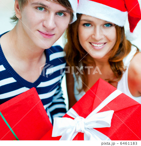 Young happy couple in Christmas hats standing together and holdi Young happy couple in Christmas hats standing together and holdi 6461183